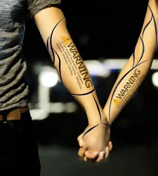 Two hands holding with warning text and designs written on their arms